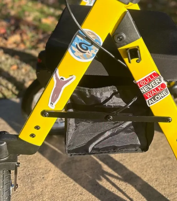 Close-up of Mellow Yellow, a bright yellow rollator covered in stickers, including a Rocky silhouette and a “You’ll Never Walk Alone” sticker.