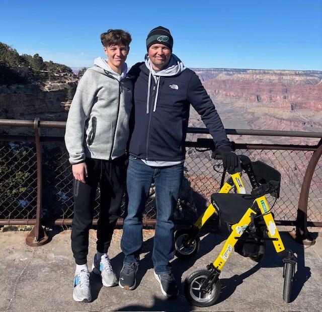 Jay and his son standing at the Grand Canyon rim with the yellow rollator beside them.