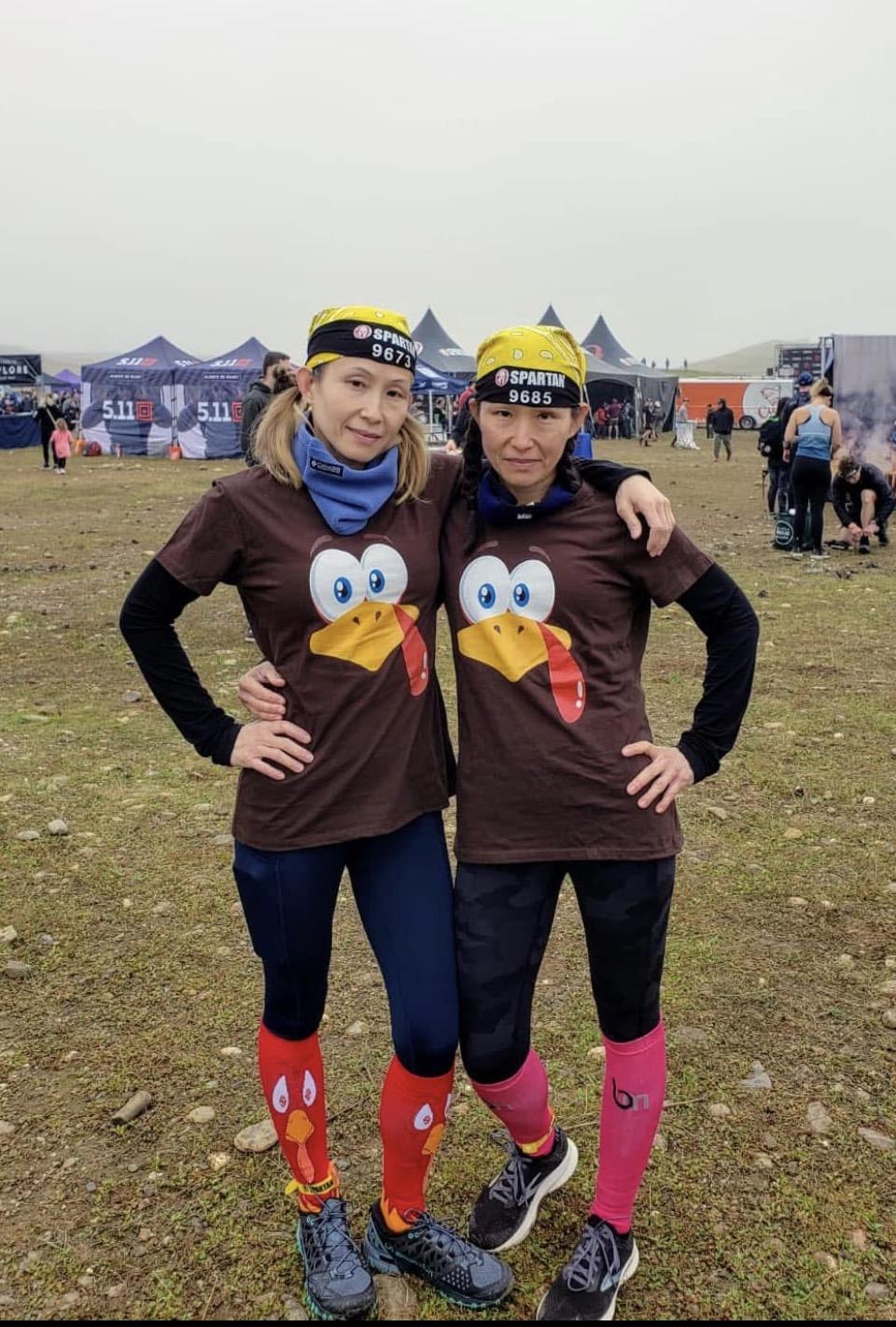 Sandy and Candy at a Spartan Race, wearing matching turkey graphic tees, race headbands, and bright compression socks.